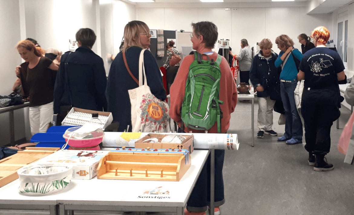Menschen in einem Raum mit Tischen mit vielen verschiedenen Dingen.
