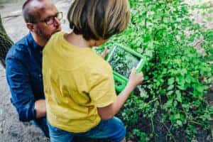Pädagogischer Mitarbeitender forscht mit Kind in der Natur.