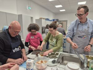 Teilnehmende der Veranstaltung "Kochen für Respekt und Vielfalt" bereiten gemeinsam ein Gericht in der vhs-Küche zu.